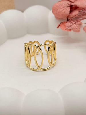 Gold ring with a geometric design on a white surface with pink flowers in the background